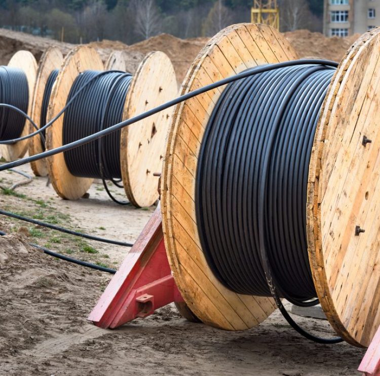 Concept of electricity supply for construction projects. Three wooden coils with power cable laid in trench.